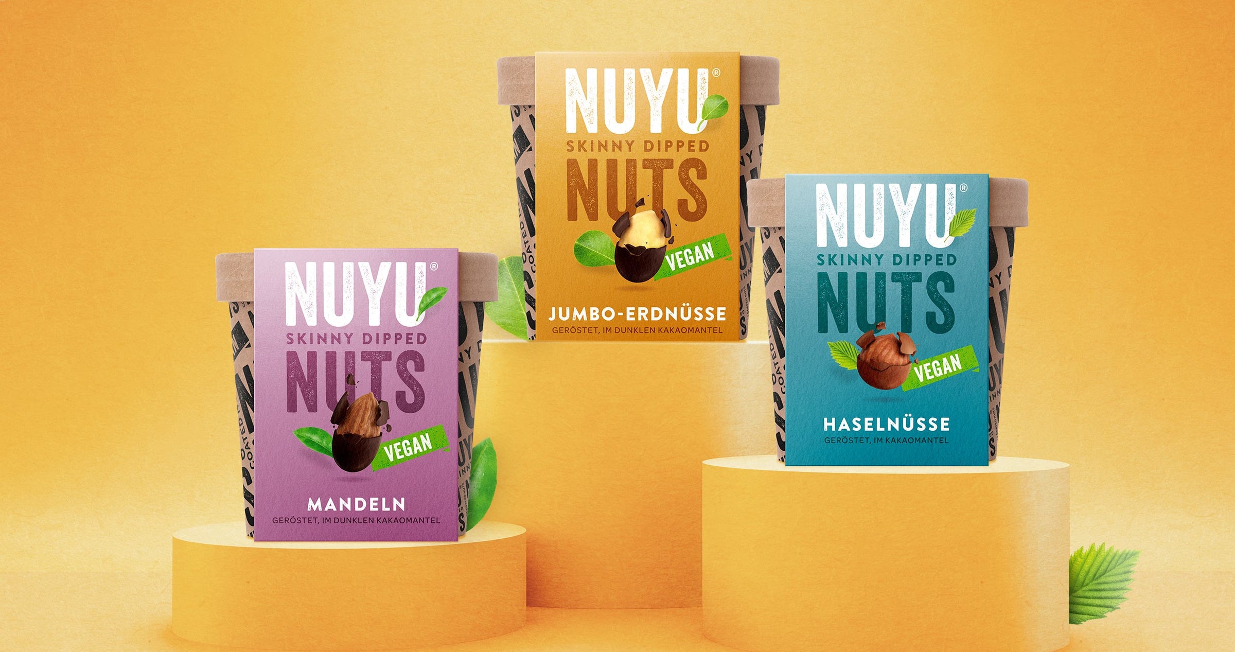 NUYU NUTS – skinny dipped Nüsse als veganer Snack: die Sorten Mandeln und Jumbo- Erdnüsse im dunklen Kakao-Mantel sowie eine Box mit Haselnüssen im Vollmilch- Schokoladen-Mantel